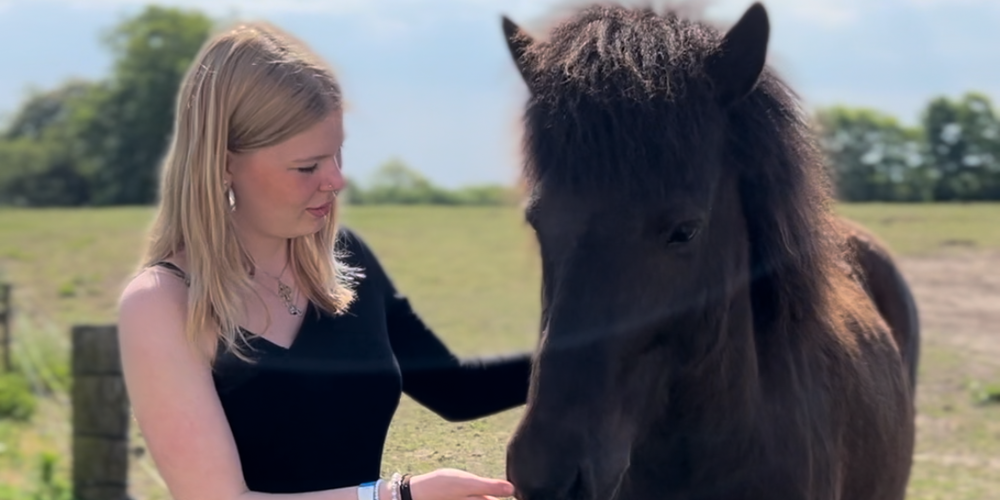 Emilie står sammen med en islænderhest i solskin